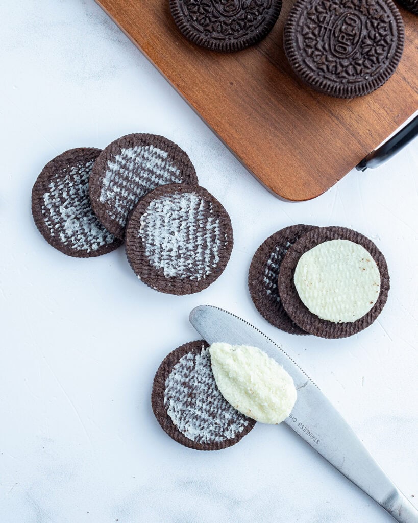 Oreo cookies broken in half with a knife removing the cream filling.