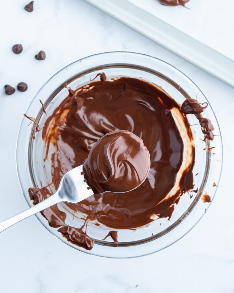Oreos dipped in melted chocolate on a fork.