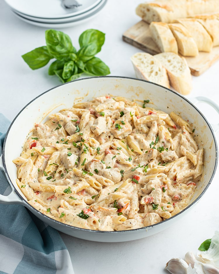 Cheesy Chicken Pasta in a pan with basil and bread behind the pan