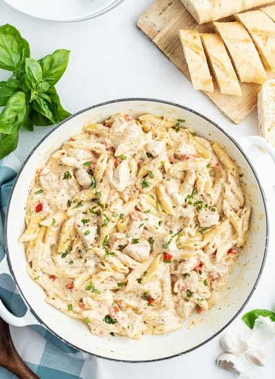 Cheesy Chicken Pasta in a pan with basil and bread behind the pan