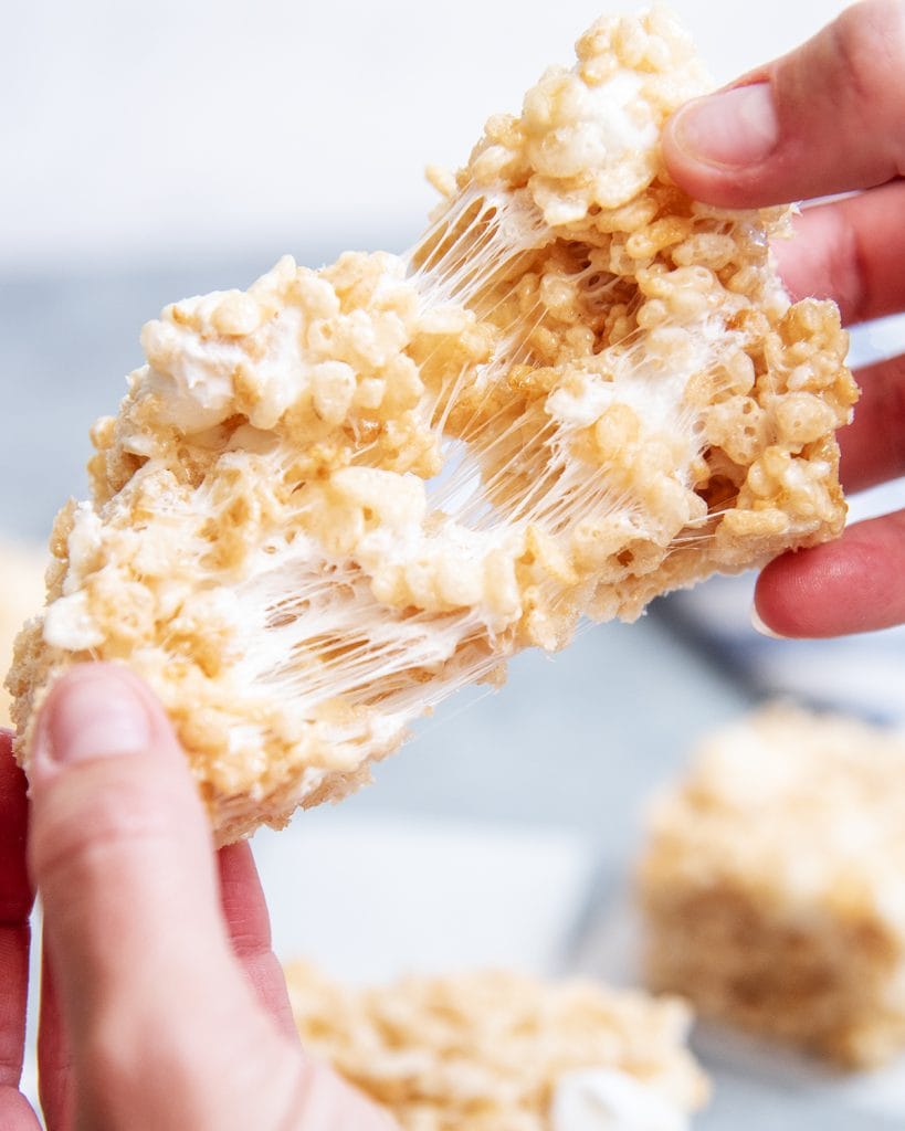 Two hands stretching a gooey marshmallow rice krispie treat between them.