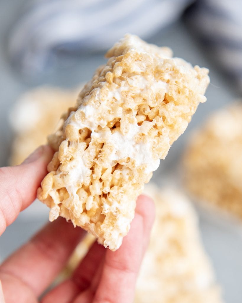 A hand holding a rice krispies treat with gooey marshmallow pieces in it.
