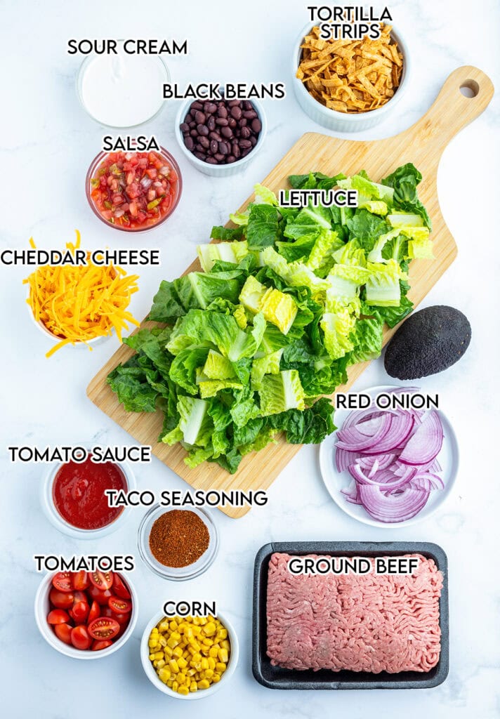 The ingredients needed to make beef taco salad in small bowls with labels above them.