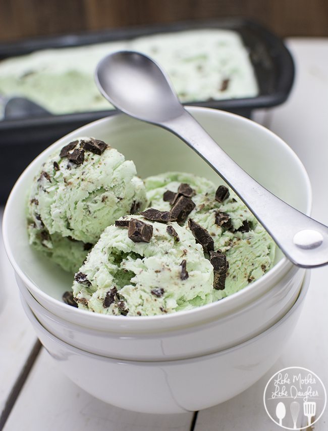 A bowl of mint ice cream topped with chopped chocolate pieces, with a spoon laying across the top.