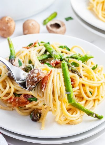 A plateful of asparagus carbonara, with a bite of it on a fork.