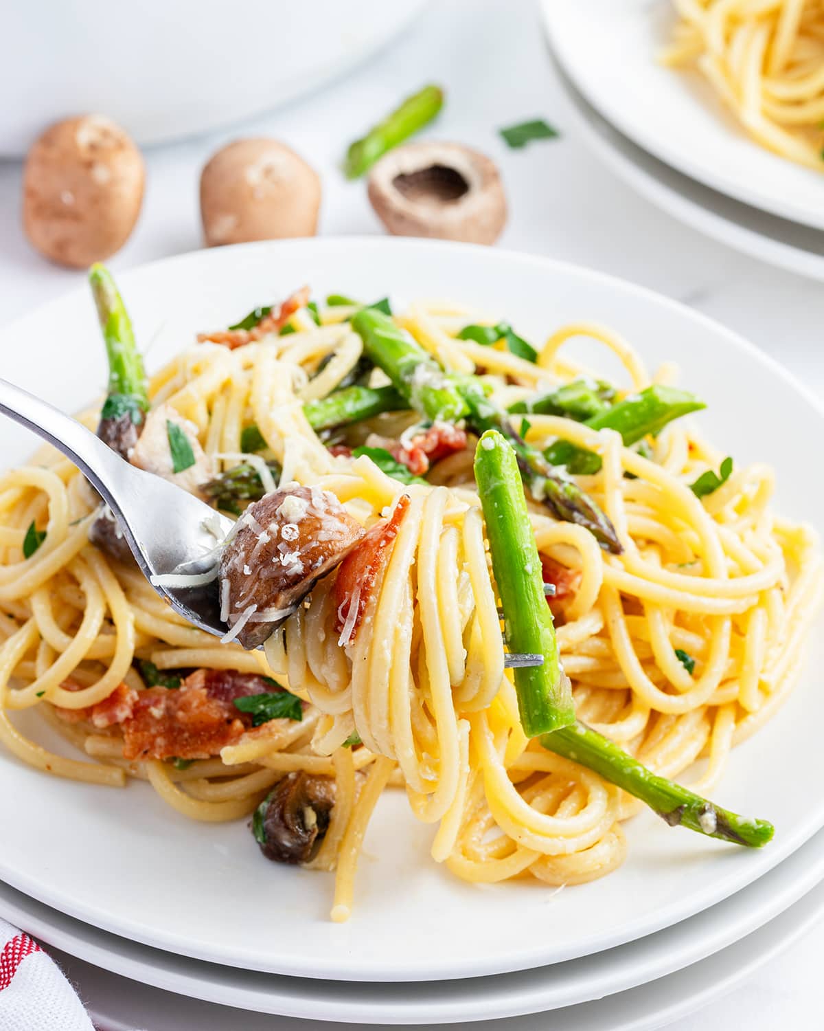A plateful of asparagus carbonara, with a bite of it on a fork.
