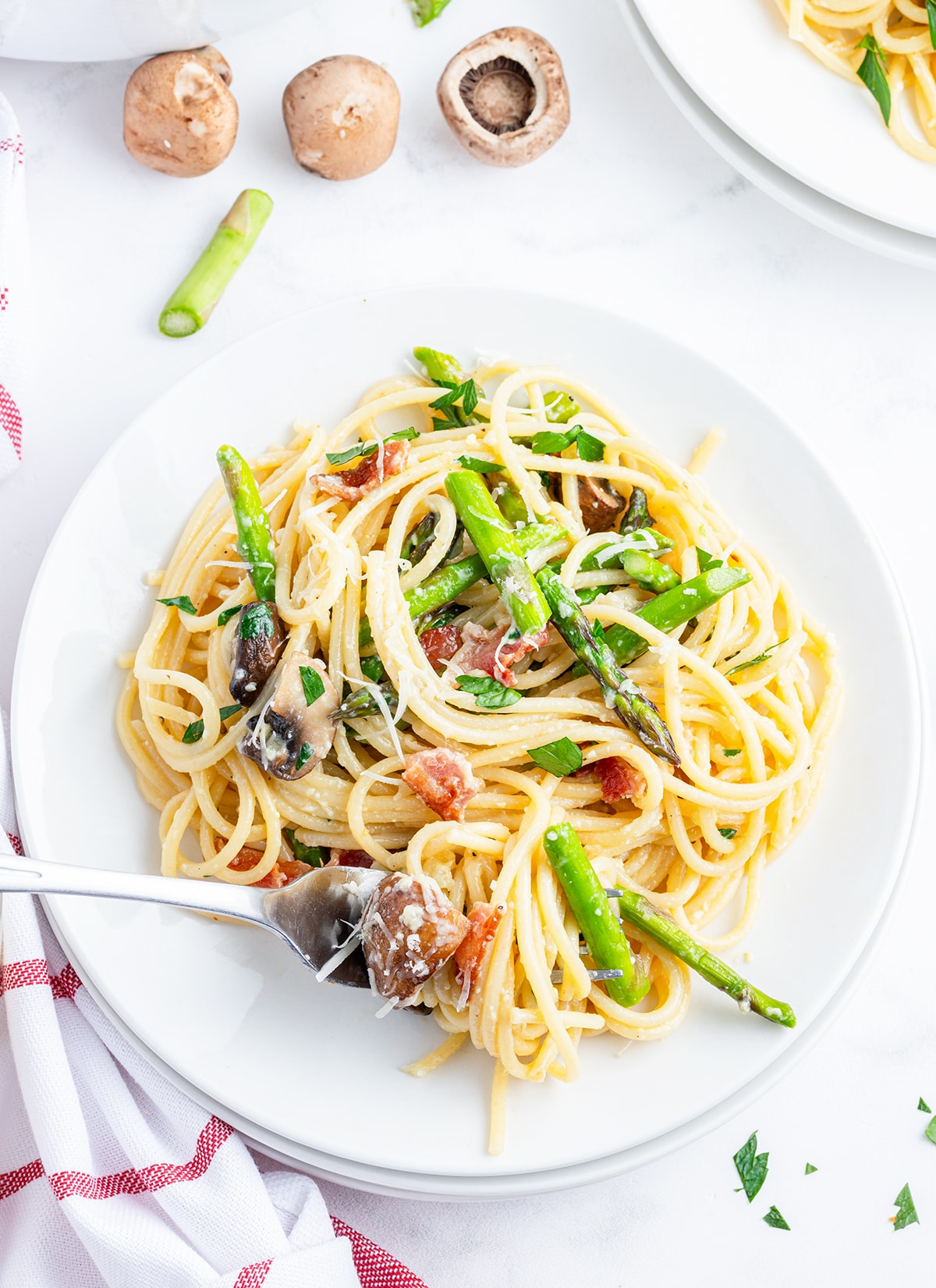 An overhead photo of a plate of asparagus carbonara pasta with bacon, asparagus, and mushrooms.