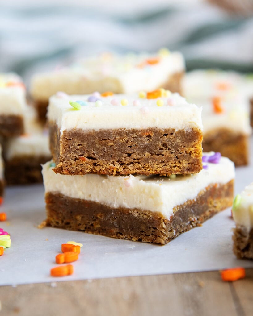 A stack of two carrot cake cookie bars with cream cheese frosting, and spring sprinkles on top.