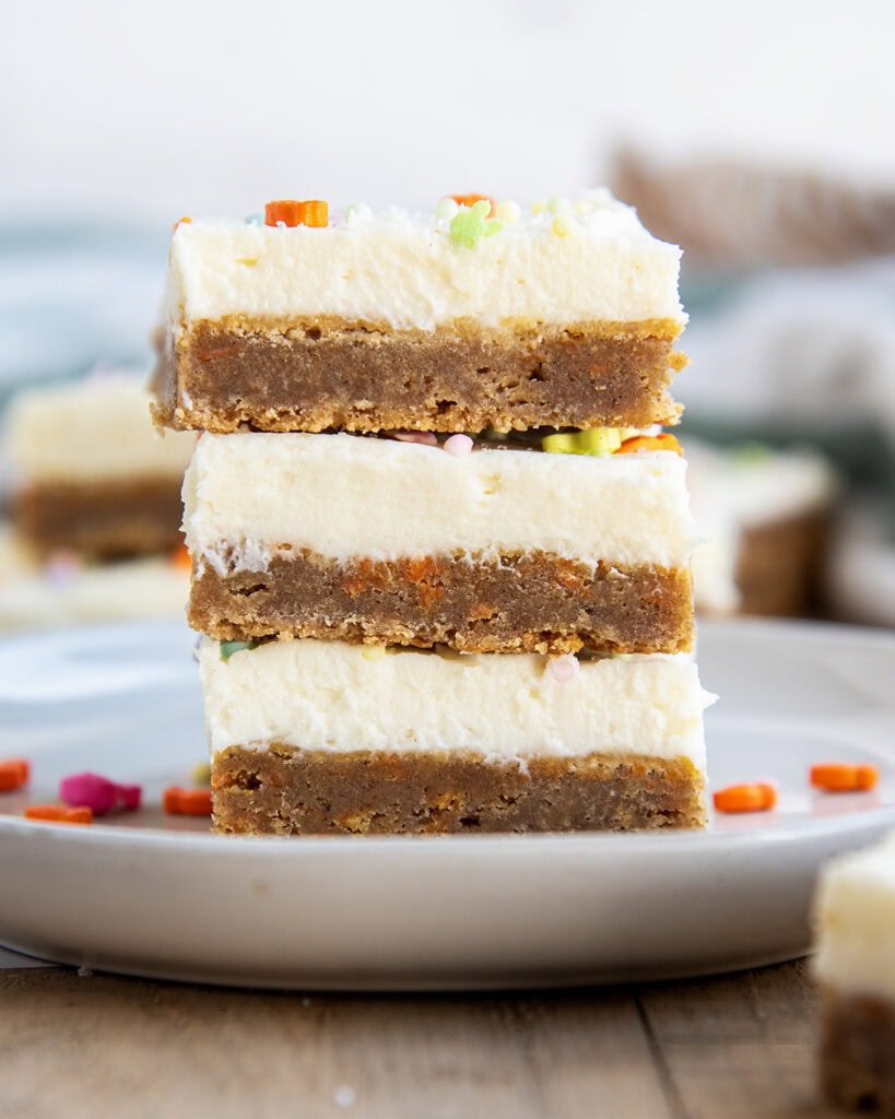 A close up of a stack of three carrot cake cookie bars each topped with cream cheese frosting.