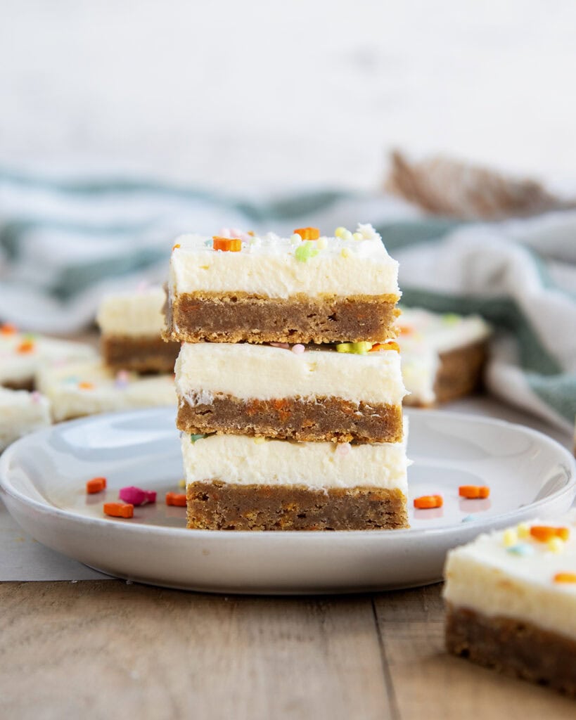 A stack of three carrot cake cookie bars each topped with cream cheese frosting.