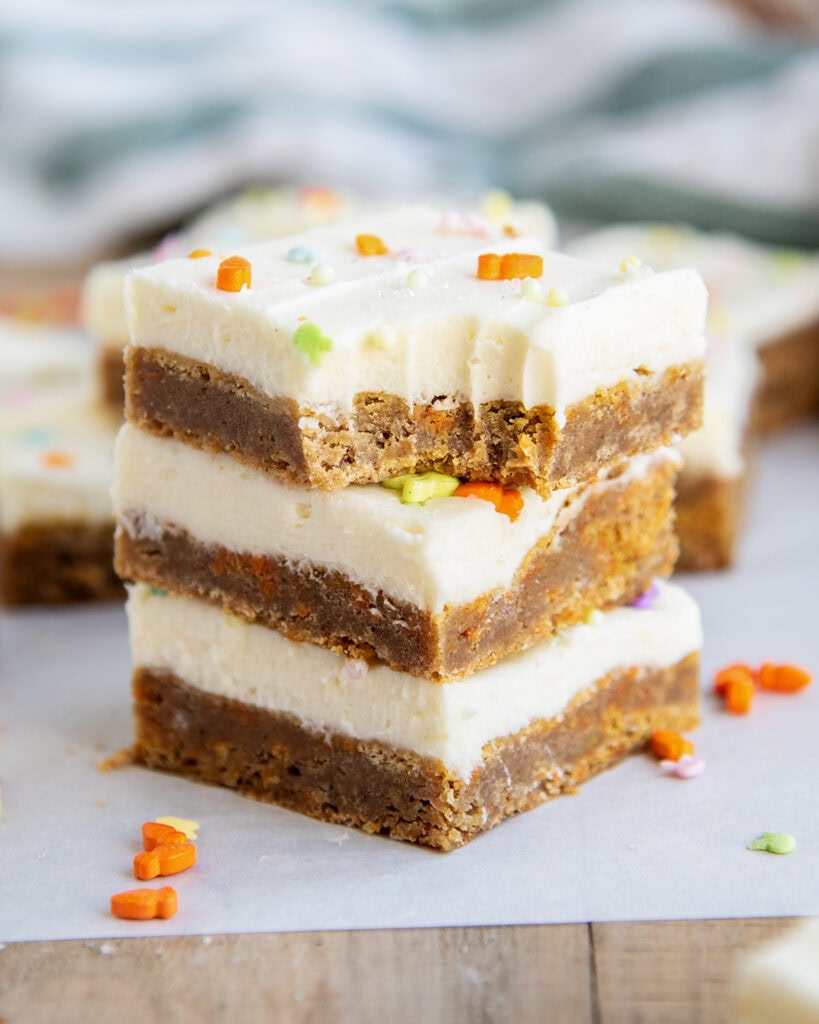A stack of three carrot cake cookie bars topped with cream cheese frosting, and the top has a bite out of it.