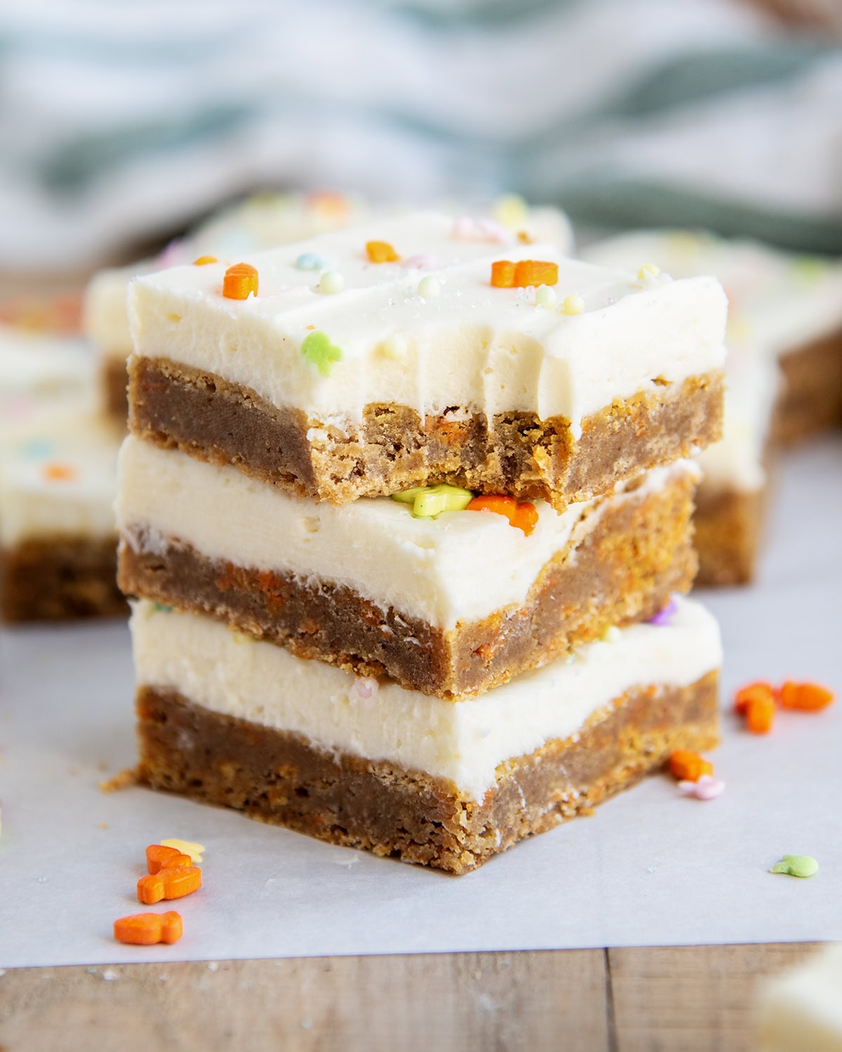 A stack of three carrot cake cookie bars topped with cream cheese frosting, and the top has a bite out of it.