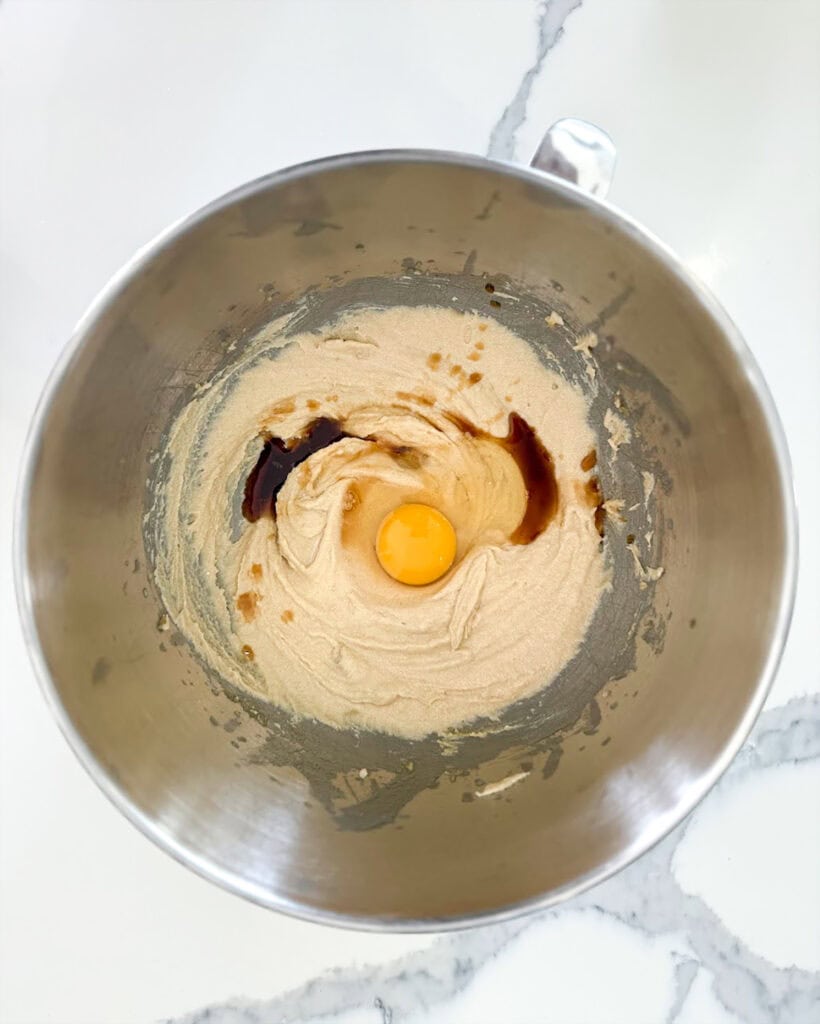 A bowl of creamed butter, topped with an egg, and vanilla extract.