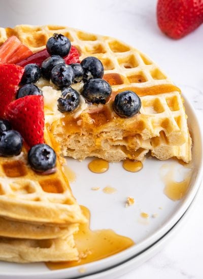 A plate of three waffles with a quarter cut out of them all. The waffles are topped with berries and syrup.