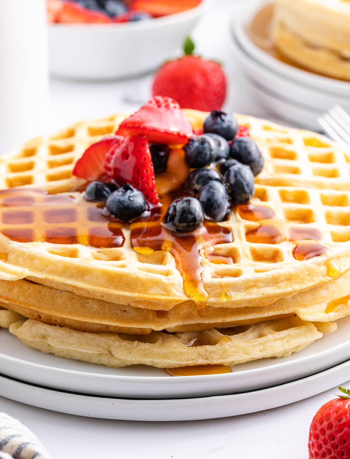 A stack of waffles on a plate topped with strawberries, blueberries, and syrup.