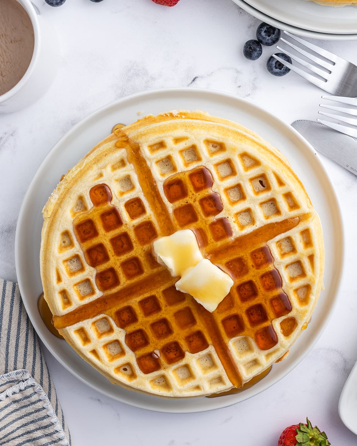 An overhead photo of a plate of waffles topped with butter squares and syrup.
