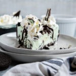 A slice of mint chocolate chip ice cream pie topped with whipped cream on a white plate.