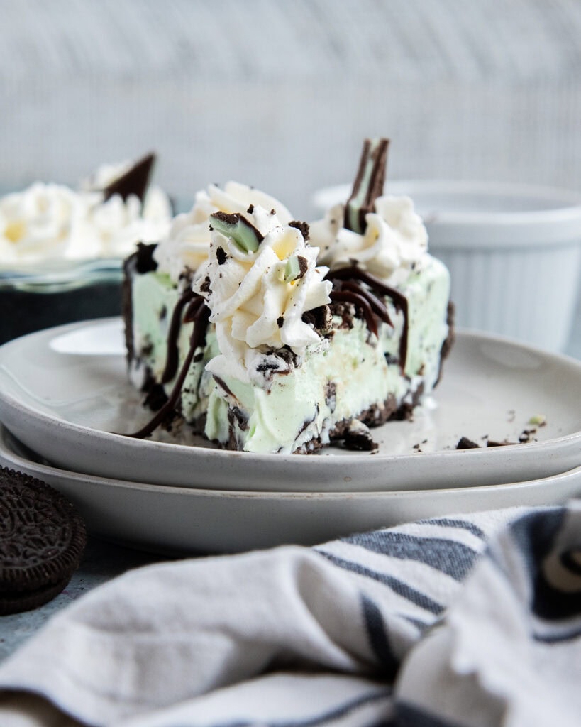 A slice of mint chocolate chip ice cream pie topped with whipped cream on a white plate.