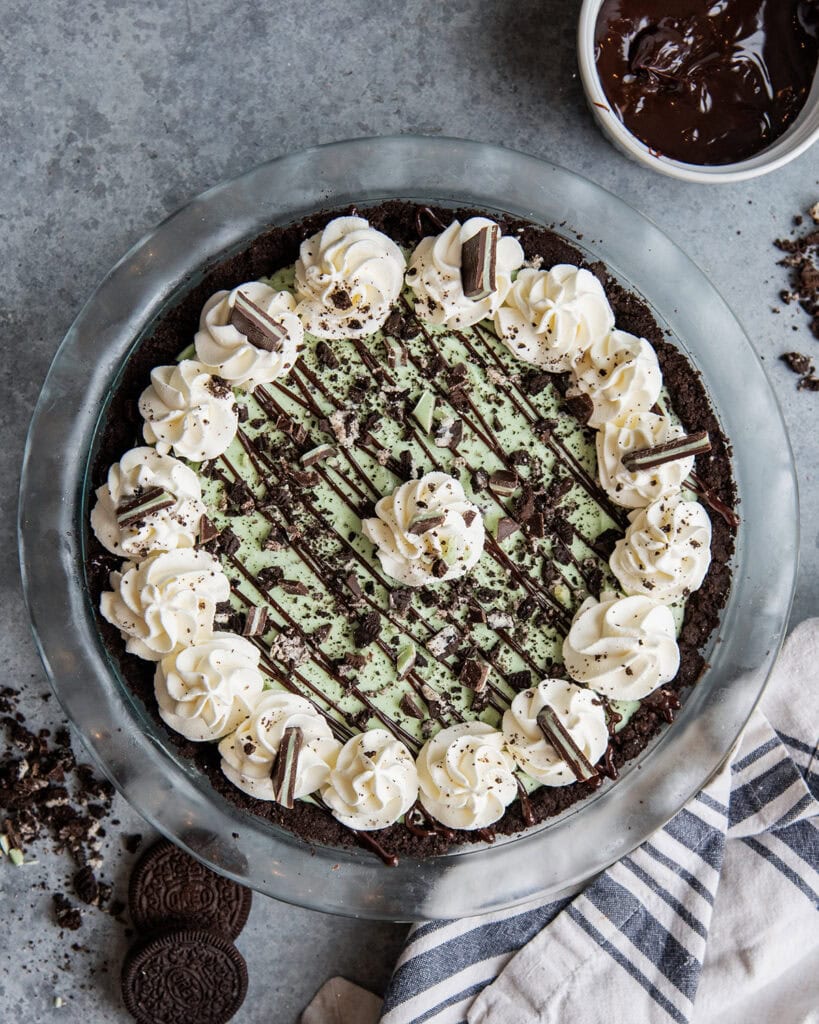 An above view of a grasshopper ice cream pie in a glass pie dish, topped with rosettes of whipped cream and Oreo cookie pieces.