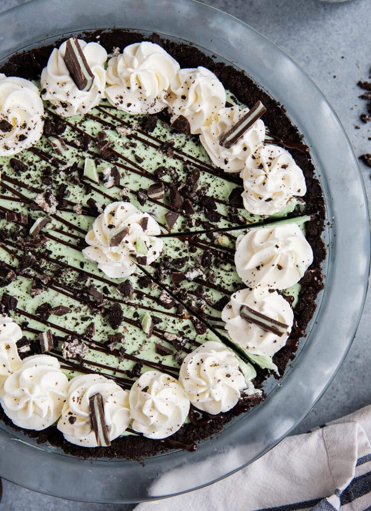 An above view of a grasshopper ice cream pie in a glass pie dish, topped with rosettes of whipped cream and Oreo cookie pieces.