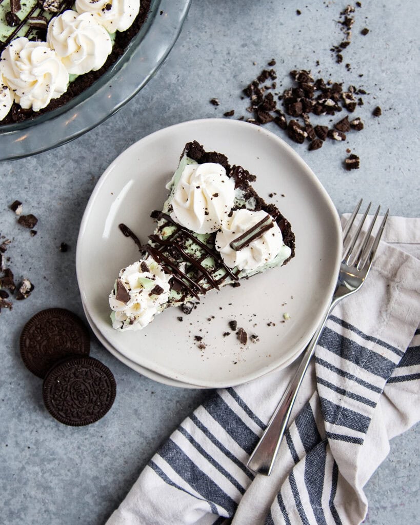 A slice of mint chocolate chip ice cream pie topped with whipped cream on a white plate.