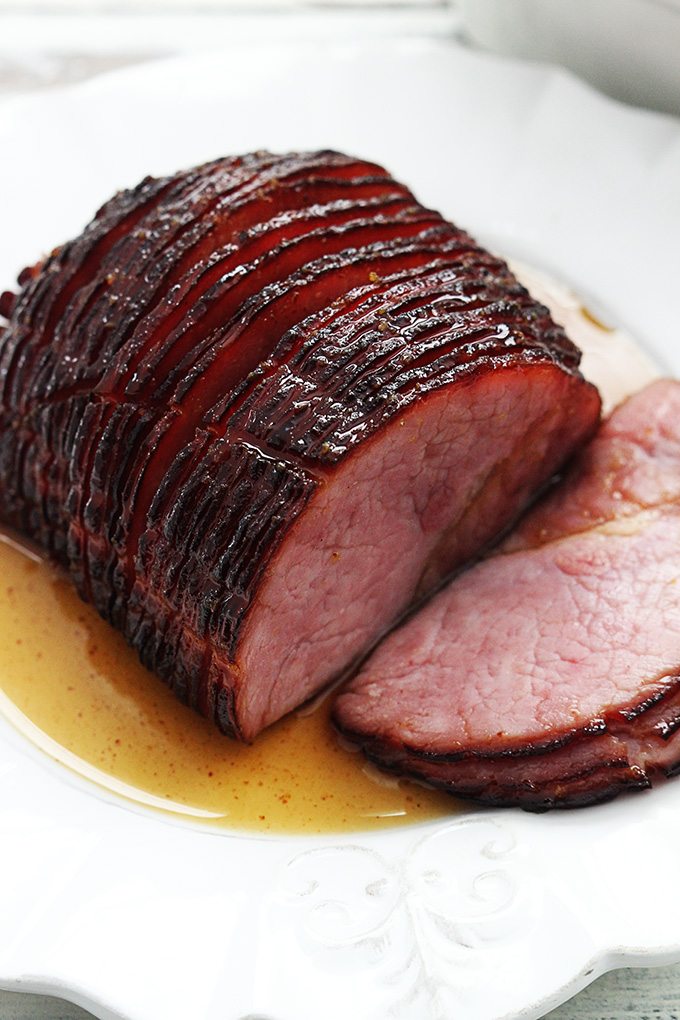 Top view of a sliced glaze ham on a white plate.