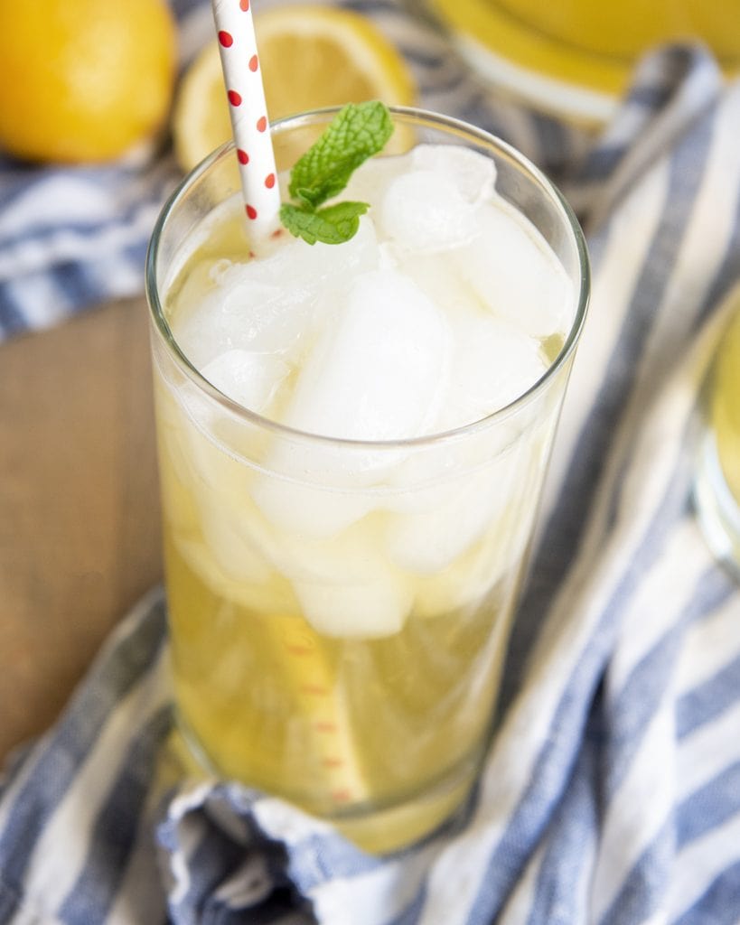 A clear glass full of lemonade and topped with ice. It has a polka dot paper straw in it, and is topped with mint leaves.