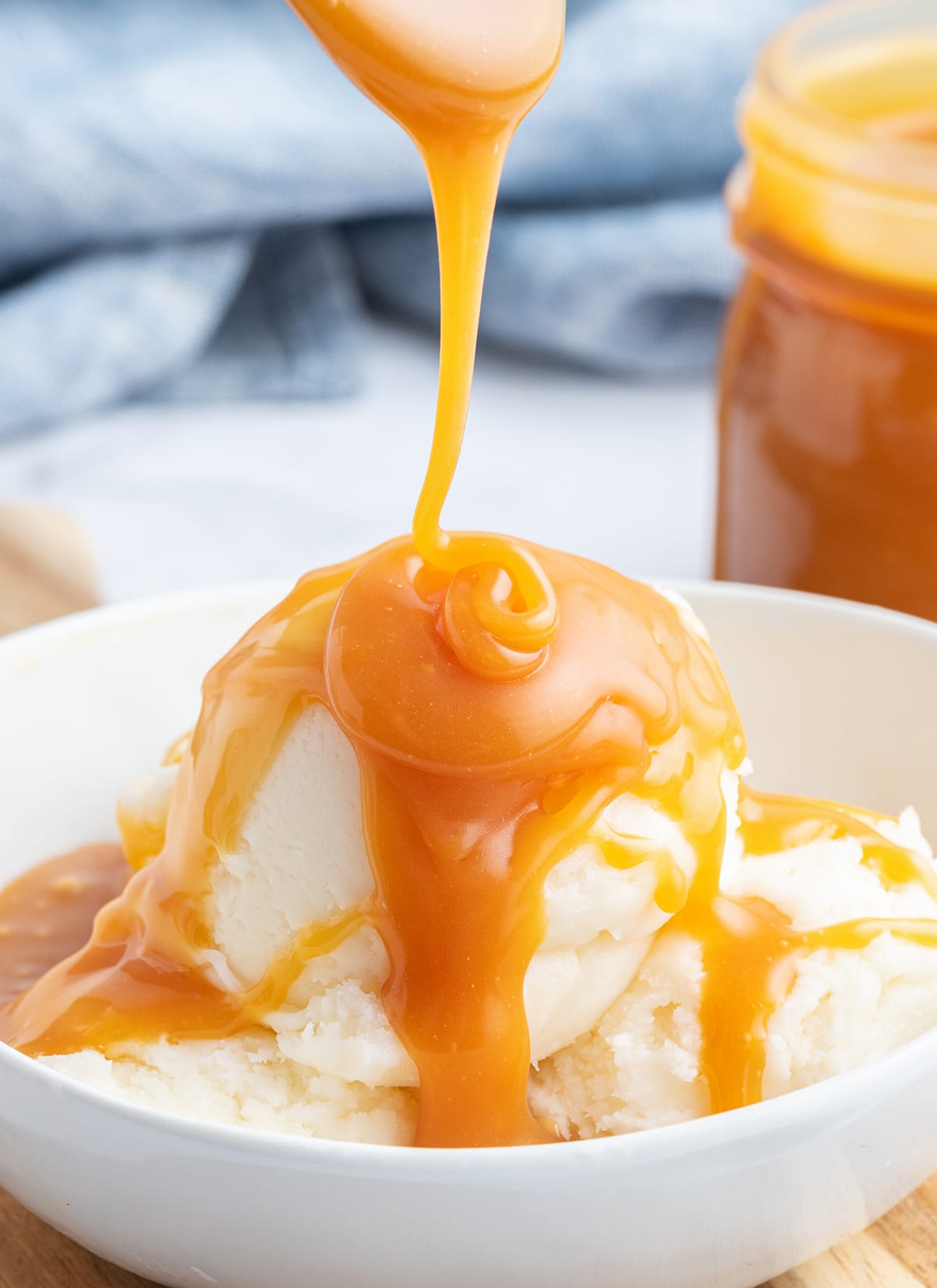 Salted caramel sauce drizzling onto a bowl of vanilla ice cream. 