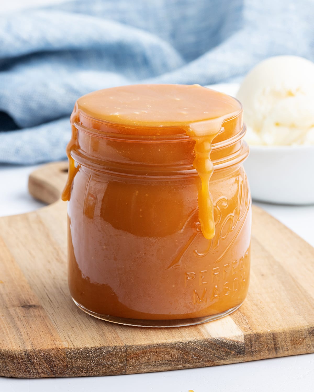A jar of homemade salted caramel sauce with the sauce drizzling over the edge of the jar.