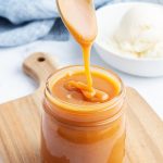 A spoonful of salted caramel drizzling into a jar of the sauce.