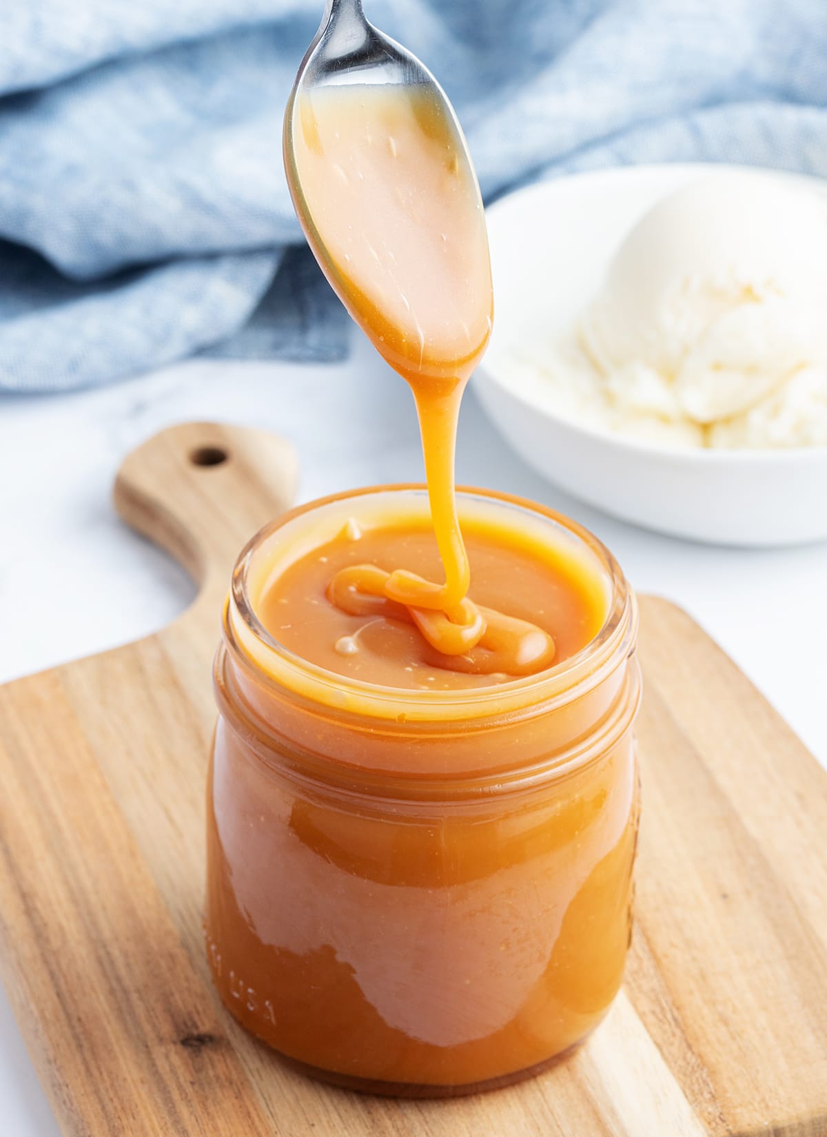 A spoonful of salted caramel drizzling into a jar of the sauce.