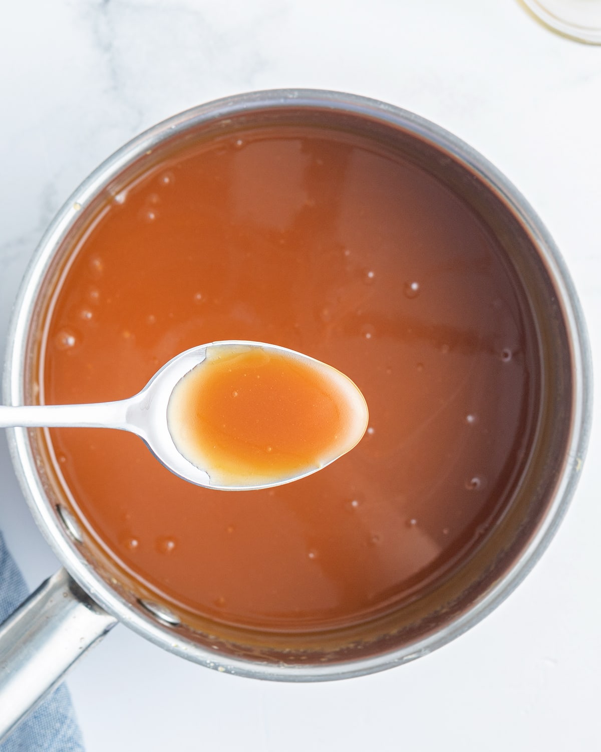 An overhead photo of a pot of salted caramel sauce with a spoonful of the sauce above it.