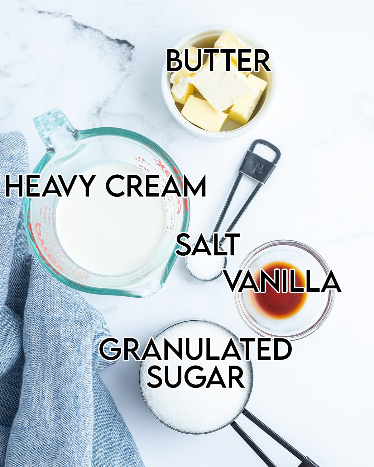 An overhead photo of the ingredients needed to make salted caramel sauce, heavy cream, butter, salt, vanilla, and granulated sugar.