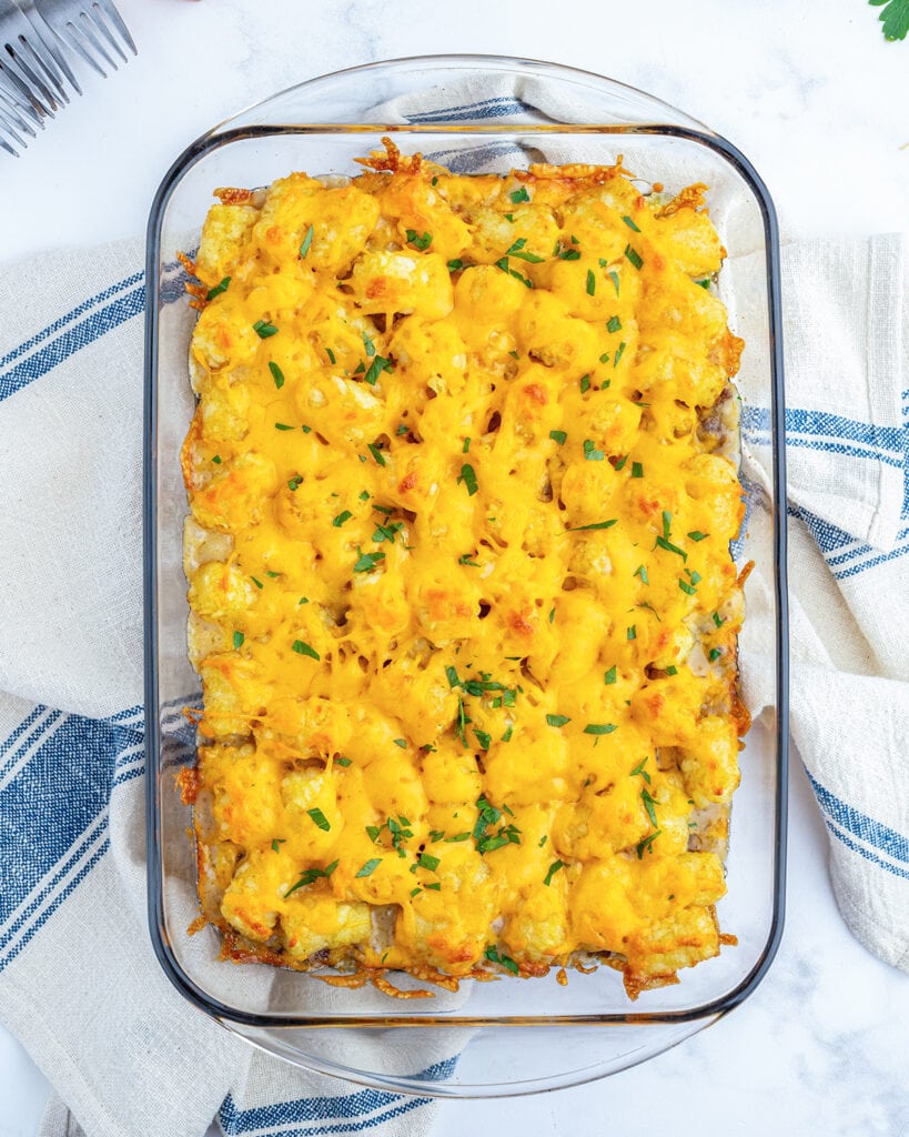 An above view of tater tot casserole topped with melted cheese and fresh parsley.