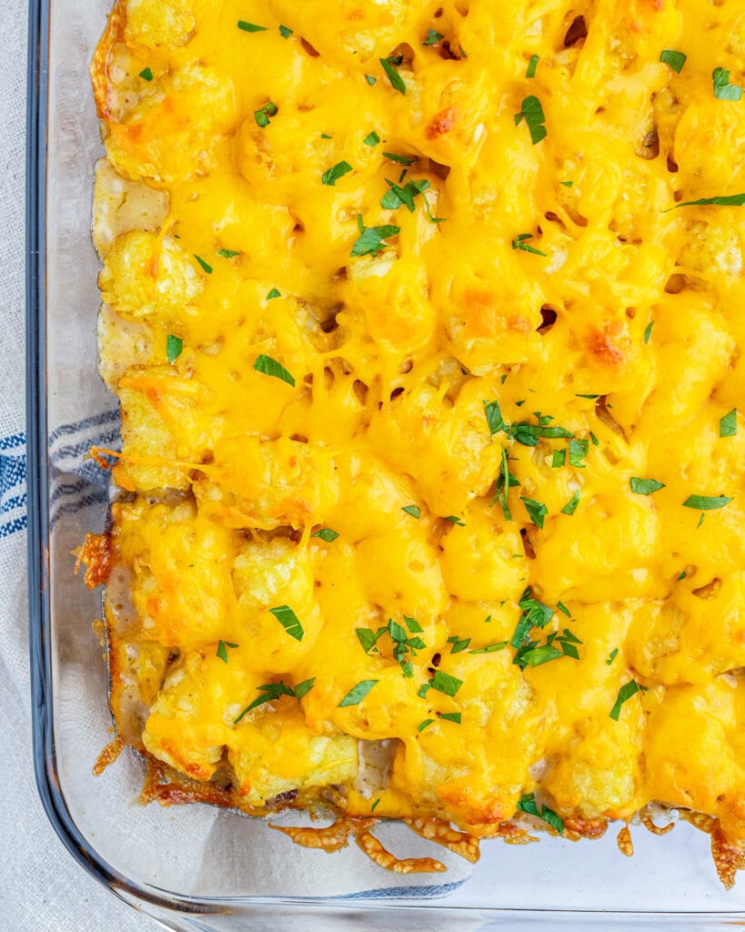 An above view of tater tot casserole topped with melted cheese and fresh parsley.