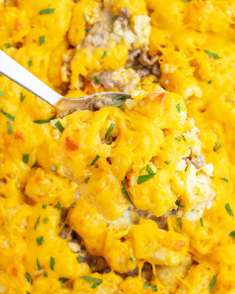 A spoonful of tater tot casserole above a pan of the casserole dish. 