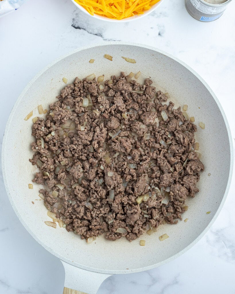 A saute pan full of browned ground beef and sauteed onions.