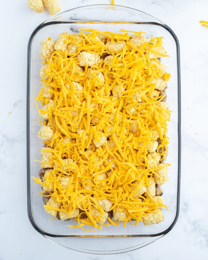 An unbaked cheeseburger tater tot casserole in a glass baking pan.