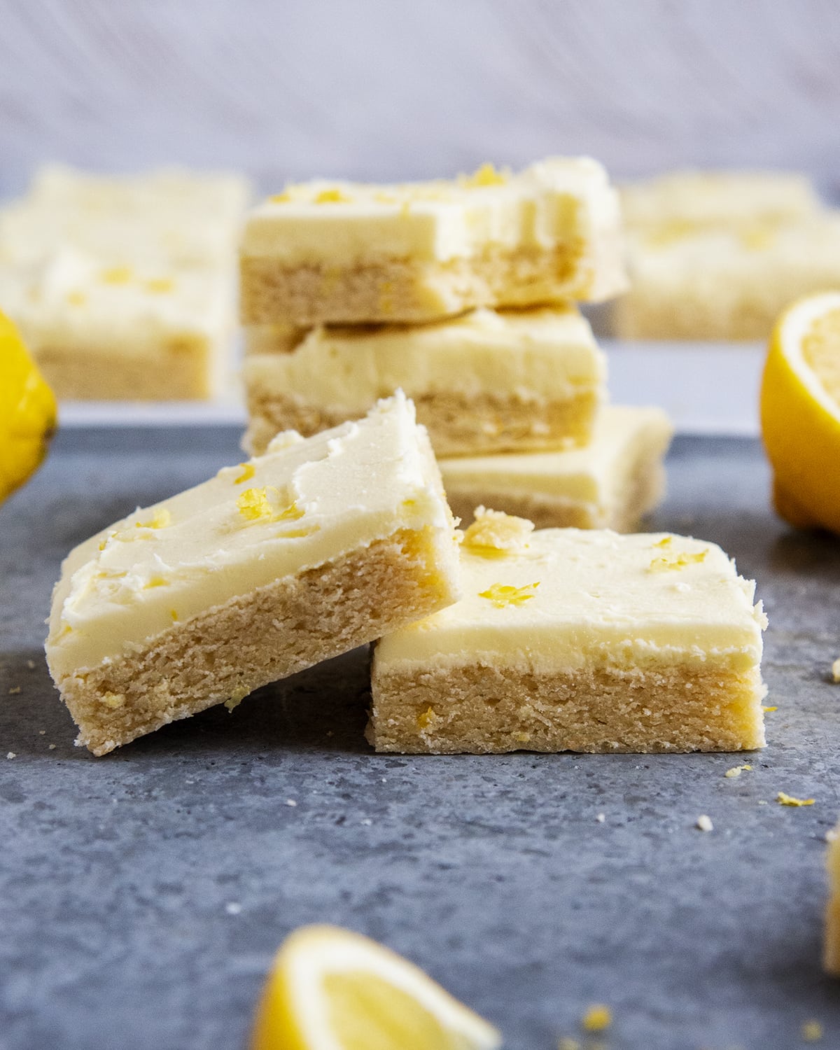 Lemon sugar cookie bars topped with lemon frosting on a gray counter top.