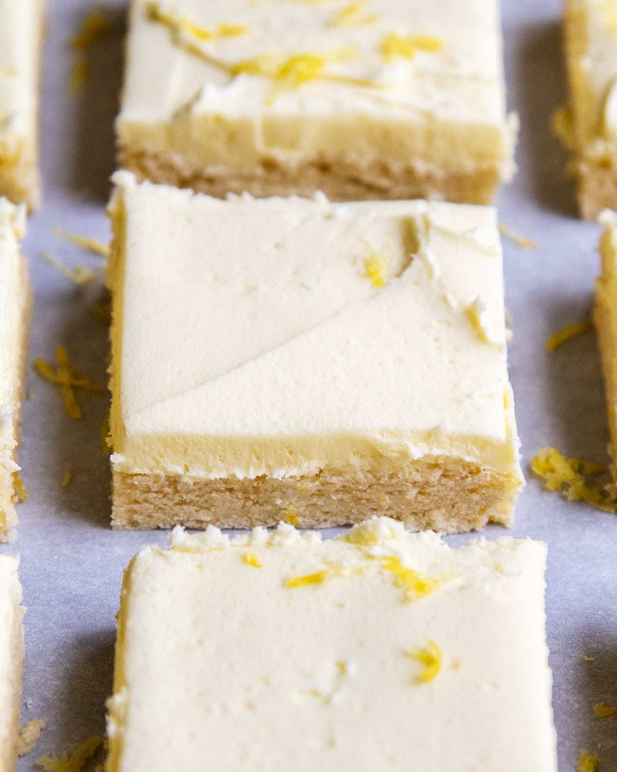 A lemon sugar cookie bar topped with frosting in a row of other sugar cookie bars.