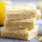 A stack of three lemon frosted sugar cookie bars topped with lemon zest.