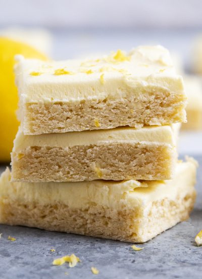 A stack of three lemon frosted sugar cookie bars topped with lemon zest.