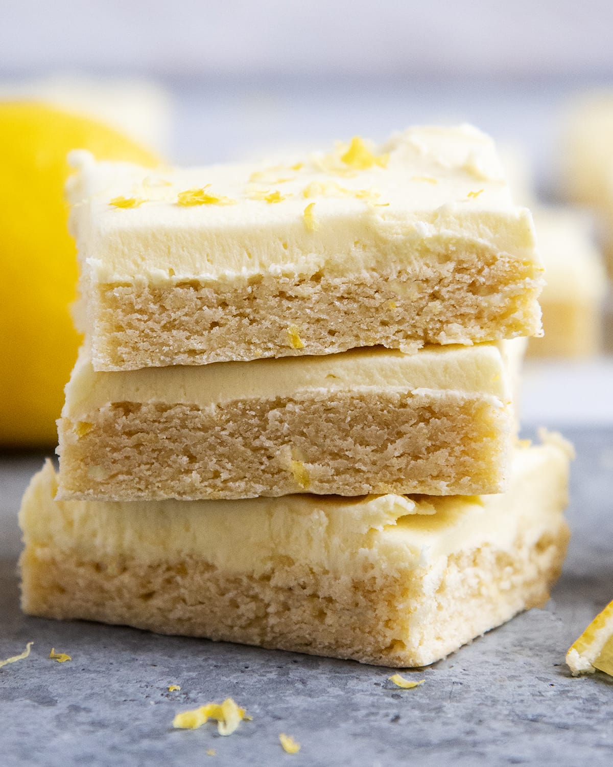 A stack of three lemon frosted sugar cookie bars topped with lemon zest.