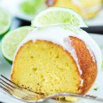 Side close up image of a slice of lime bundt cake with frosting on top and lime wedge.