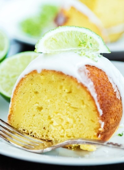 Side close up image of a slice of lime bundt cake with frosting on top and lime wedge.