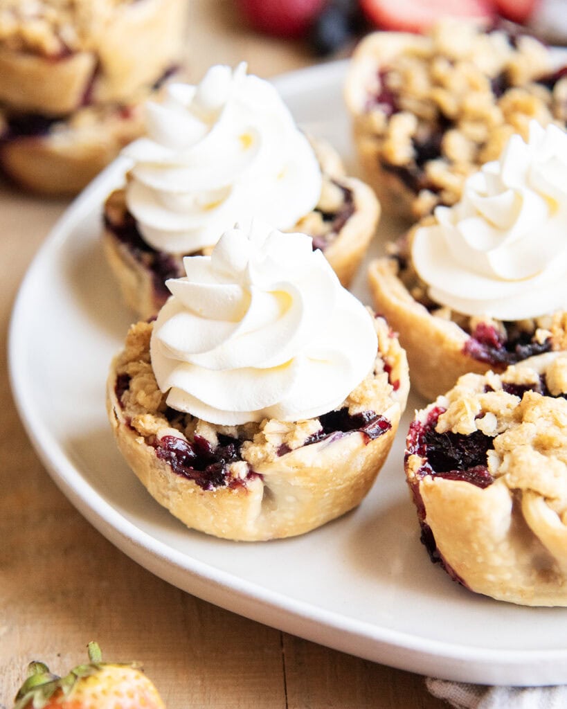 A plate of mini berry pies topped with whipped cream dollops.