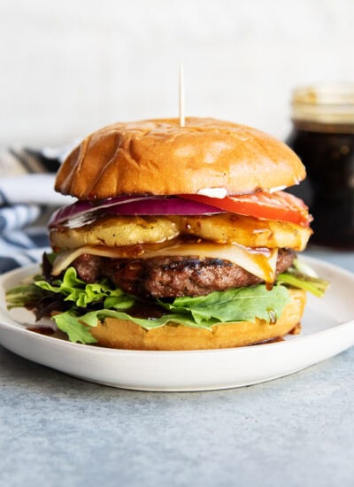 A teriyaki cheeseburger on a plate with pineapple, tomato, and lettuce on it.