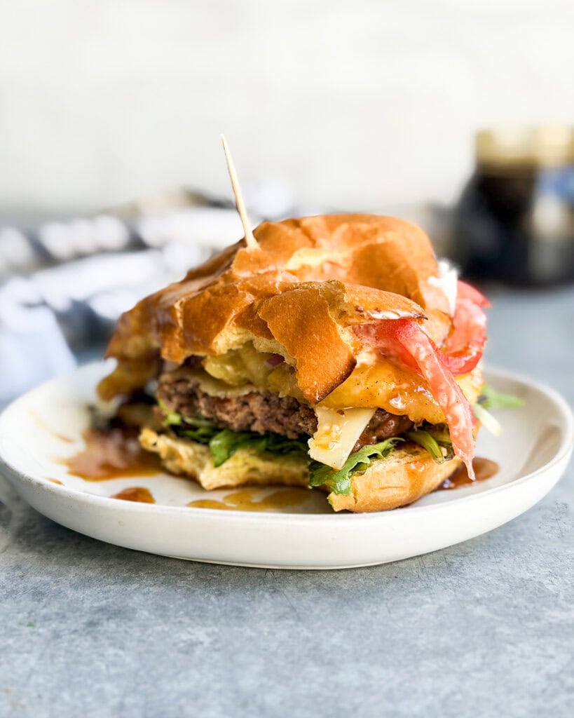 A teriyaki burger on a plate with bites out of it. 