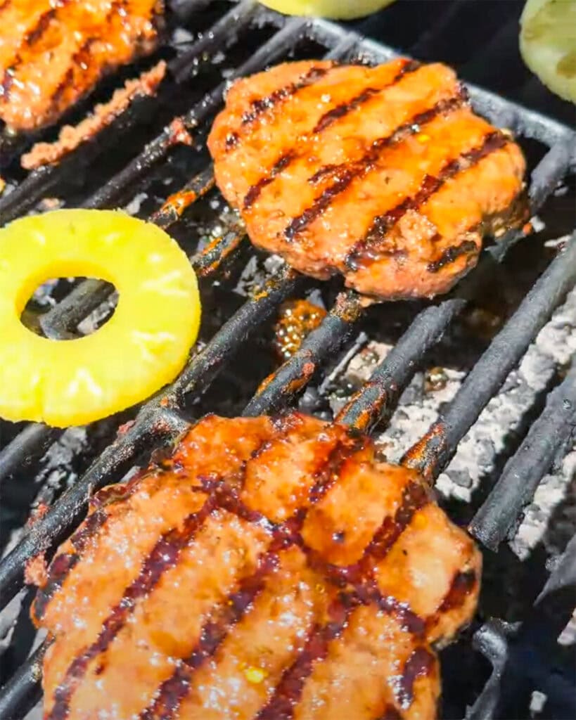 Burgers and pineapple slices cooking on a grill.