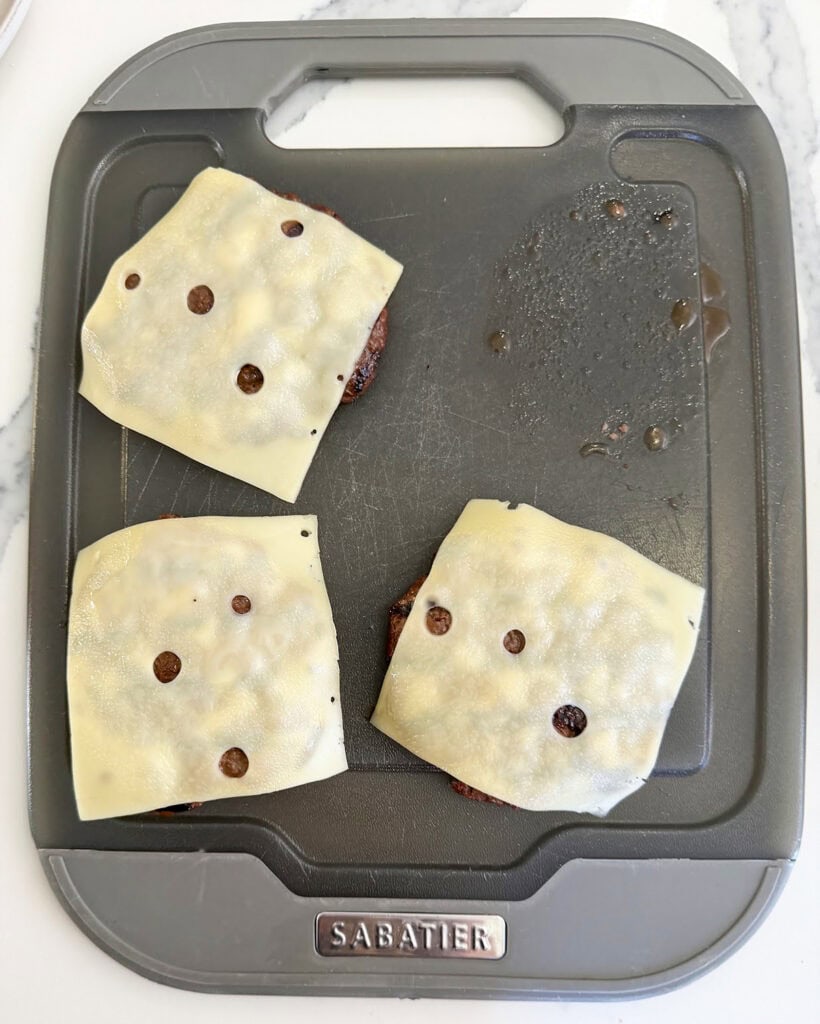 Three burger patties topped with swiss cheese.